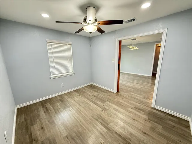 an empty room with wooden floor fan and windows