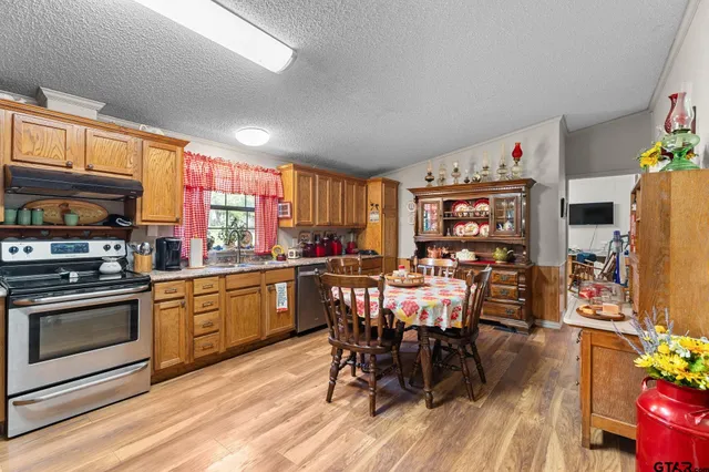 a kitchen with stainless steel appliances granite countertop a stove a refrigerator a kitchen island a dining table and chairs with wooden floor