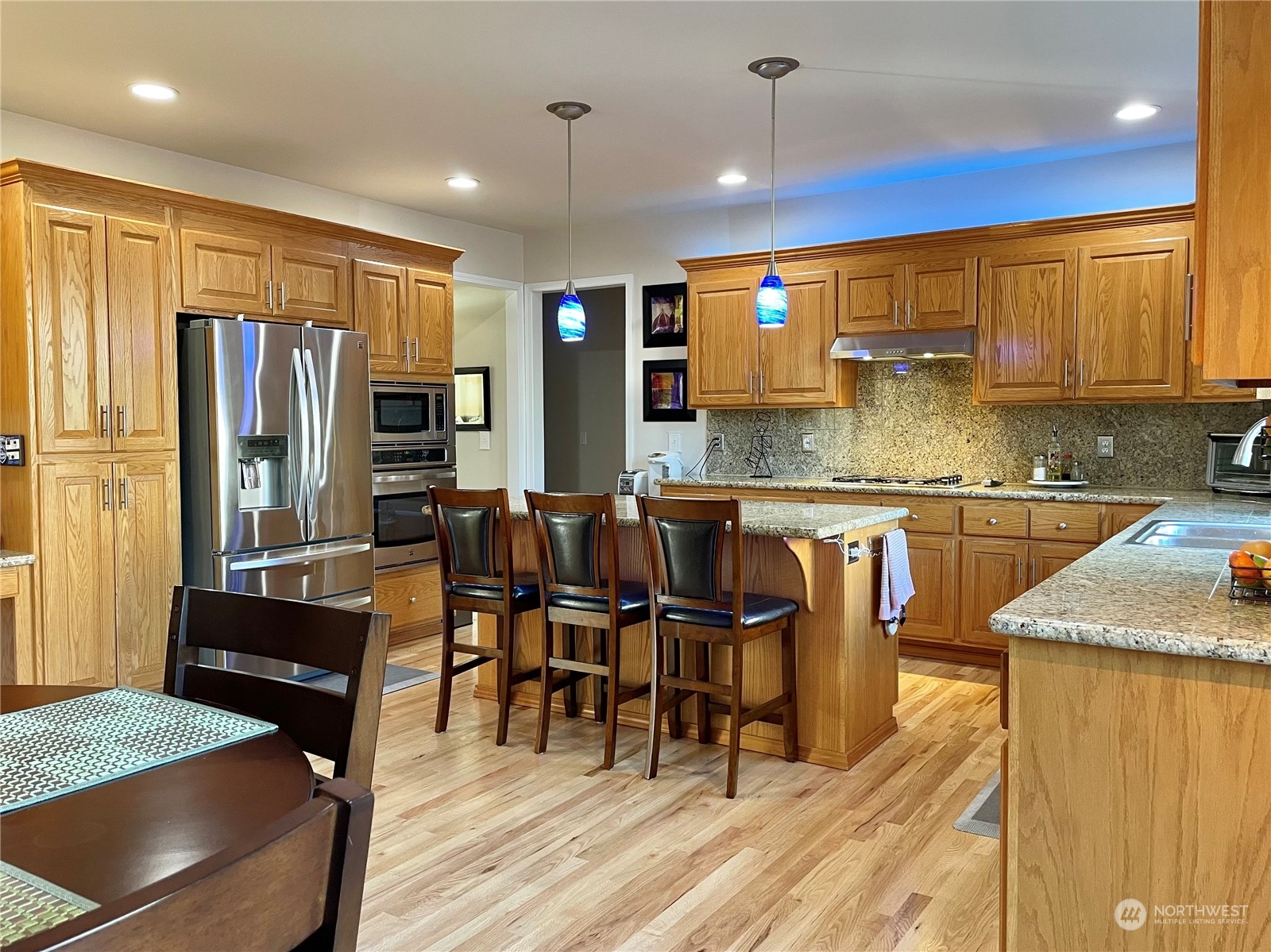 113 181st Street Southwest Bothell, WA 98012 - Photo 8 of 26 a kitchen with stainless steel appliances granite countertop a stove top oven a sink a dining table and chairs with wooden floor