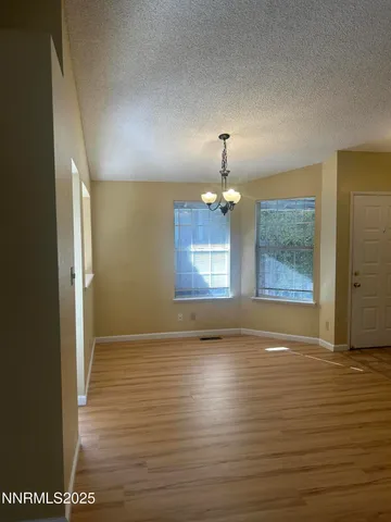an empty room with wooden floor chandelier and windows