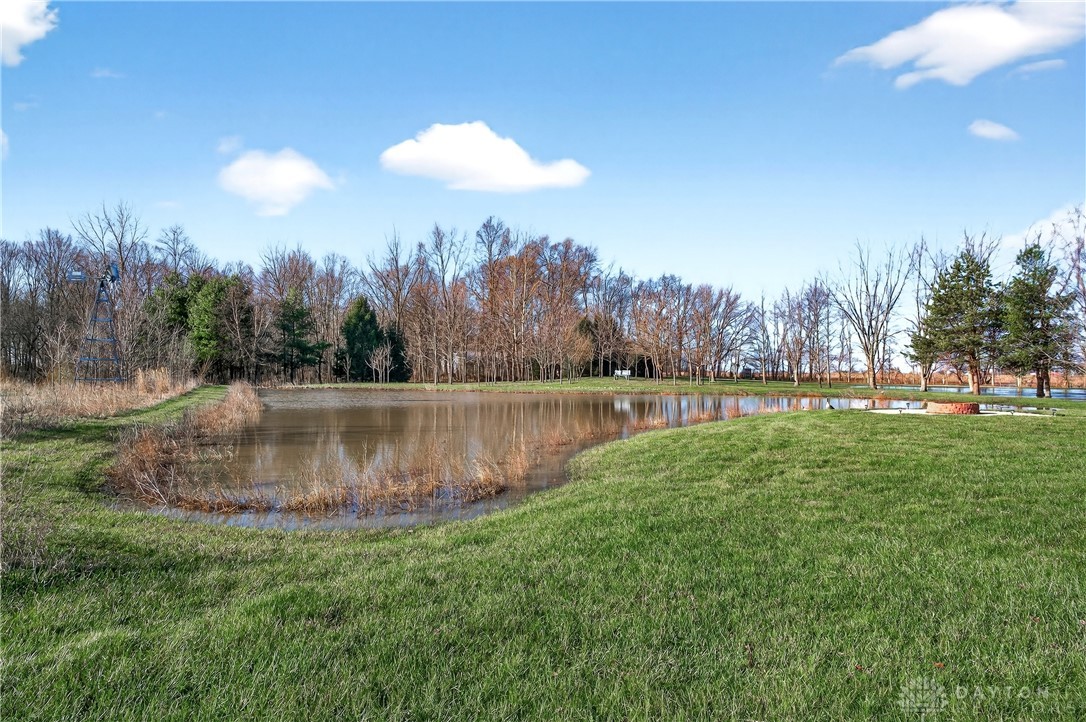 6560 Snyder Road Fletcher, OH 45326 - Photo 45 of 71 This expansive lot features a serene pond, lush green grass, and mature trees under a clear blue sky.