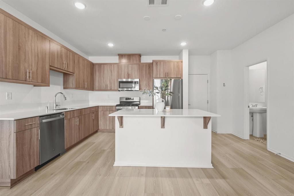 a large kitchen with stainless steel appliances granite countertop a stove a sink a refrigerator and white cabinets with wooden floor