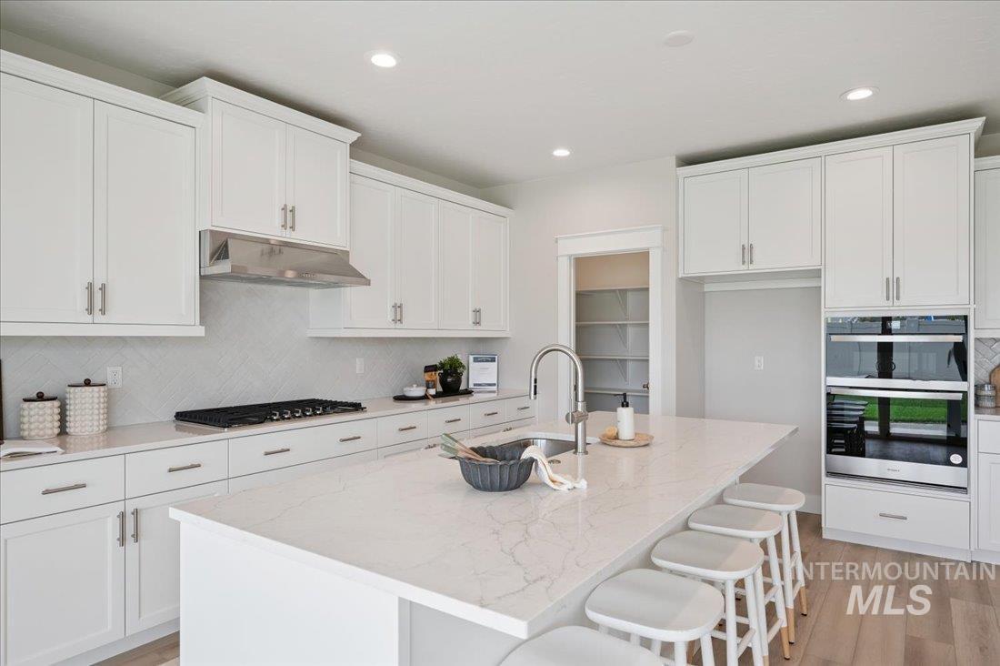 6271 West Snow Currant Street Meridian, ID 83646 - Photo 6 of 14 Kitchen featuring decorative backsplash, light stone counters, light wood-type flooring, a kitchen island with sink, and a kitchen breakfast bar