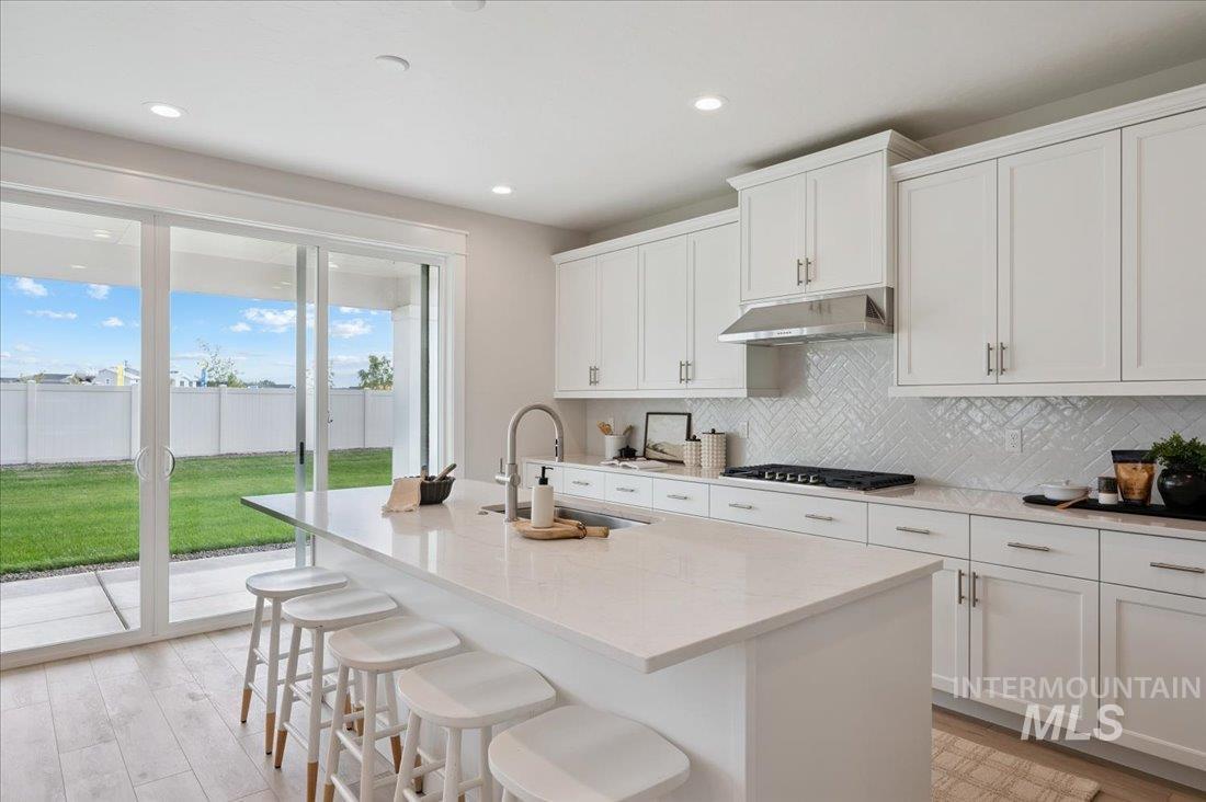 6271 West Snow Currant Street Meridian, ID 83646 - Photo 7 of 14 Kitchen featuring a kitchen breakfast bar, light stone countertops, a center island with sink, white cabinets, and light wood-style floors