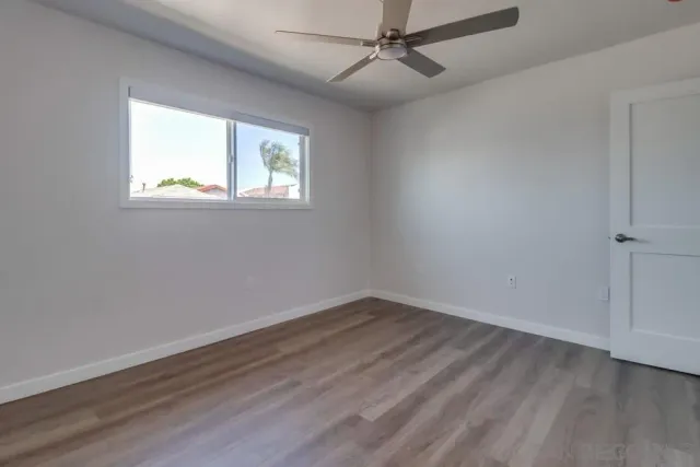an empty room with wooden floor fan and windows