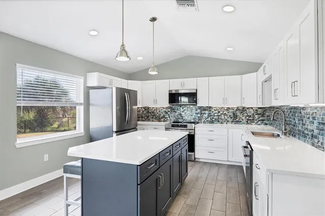 a kitchen that has a lot of white cabinets and stainless steel appliances