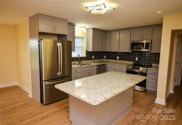a kitchen with stainless steel appliances granite countertop a refrigerator a stove a sink cabinets and wooden floor