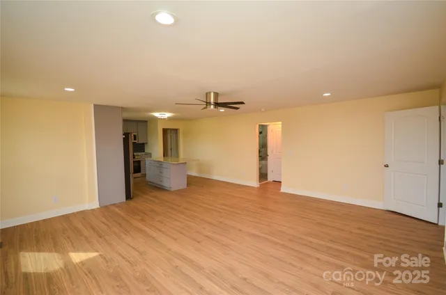 a view of a big room with wooden floor a ceiling fan and kitchen view