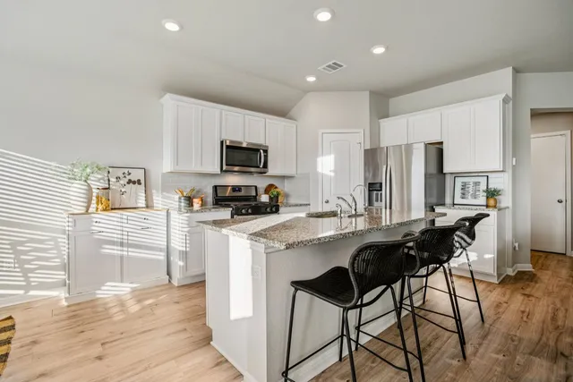 a kitchen with stainless steel appliances a stove a refrigerator a sink a stove a refrigerator and white cabinets with wooden floor