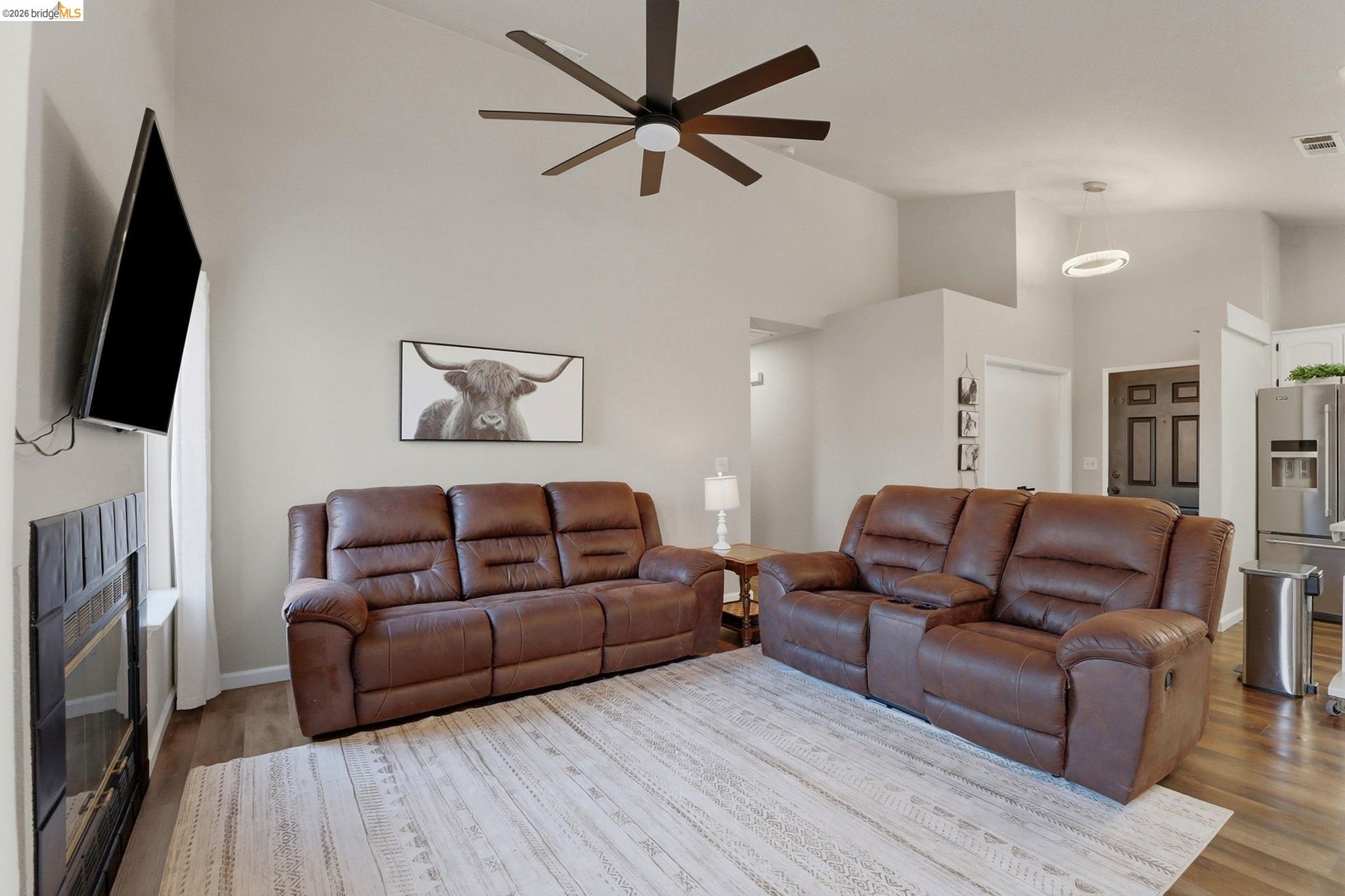 799 Morgans Ranch Circle Galt, CA 95632 - Photo 7 of 36 Living area featuring a glass covered fireplace, wood finished floors, vaulted ceiling, and a ceiling fan