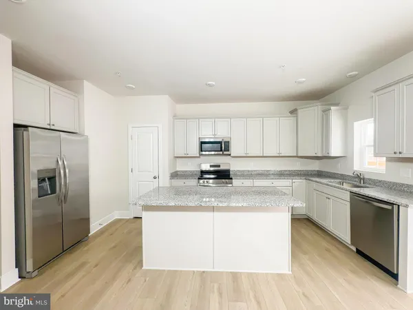 a kitchen with stainless steel appliances granite countertop a stove a sink dishwasher a refrigerator and white cabinets with wooden floor