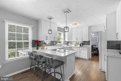 a kitchen with stainless steel appliances granite countertop a refrigerator a sink dishwasher a stove and white cabinets with wooden floor