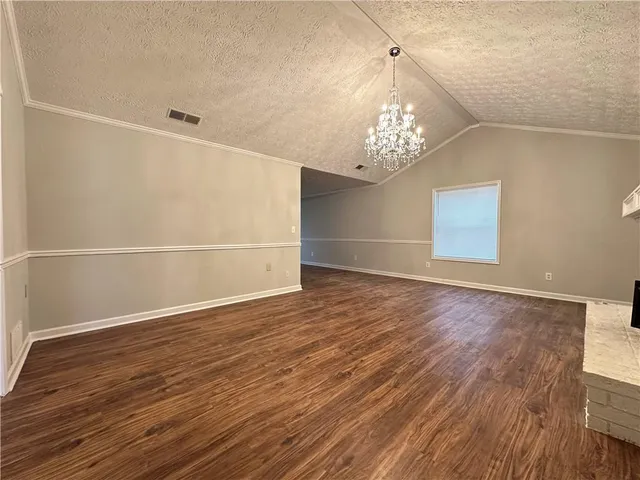 an empty room with wooden floor chandelier and windows