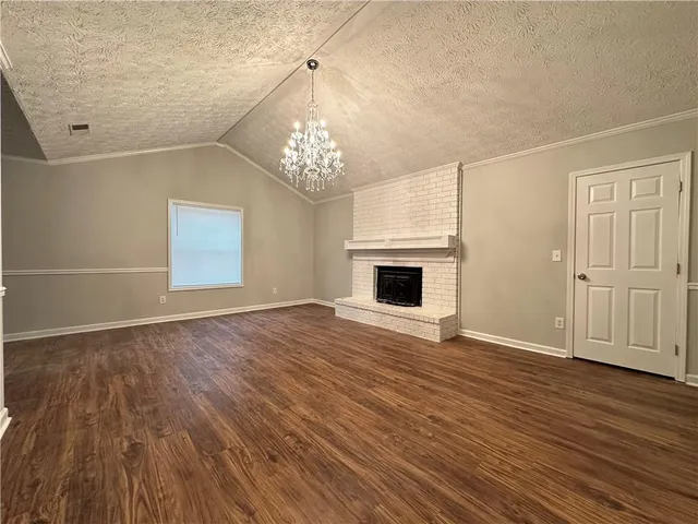 an empty room with wooden floor chandelier and windows