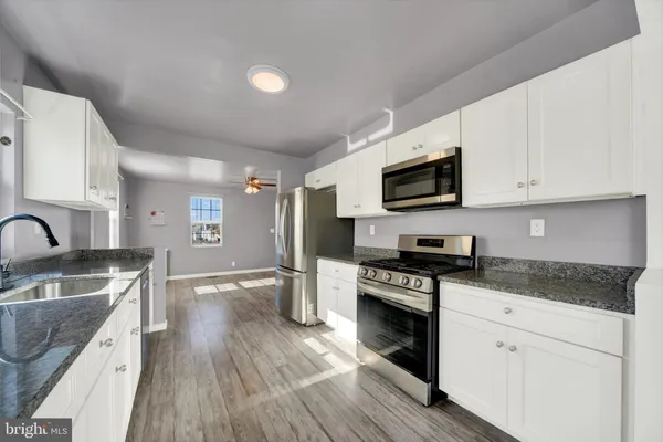 a kitchen with granite countertop a stove top oven a sink dishwasher and white cabinets with wooden floor