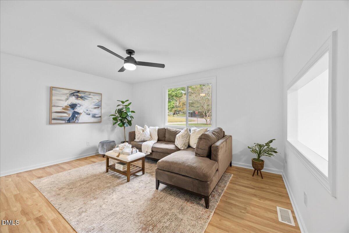 3437 Apache Drive Raleigh, NC 27609 - Photo 9 of 40 Bright living area featuring wood-finish flooring, a ceiling fan with integrated lighting, and a large window