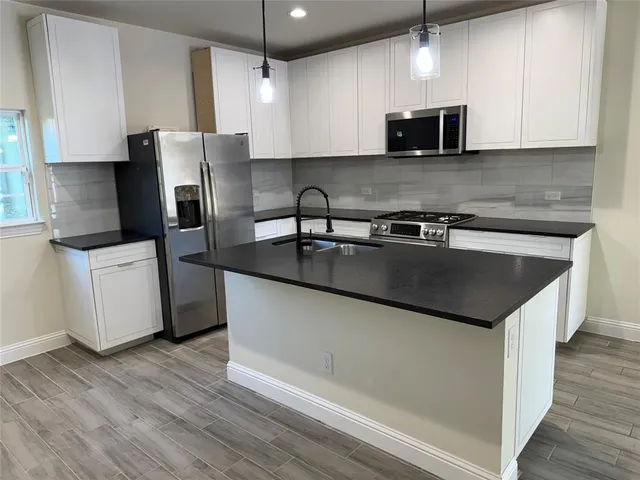 a kitchen with stainless steel appliances granite countertop a sink a stove a refrigerator a microwave oven with white cabinets