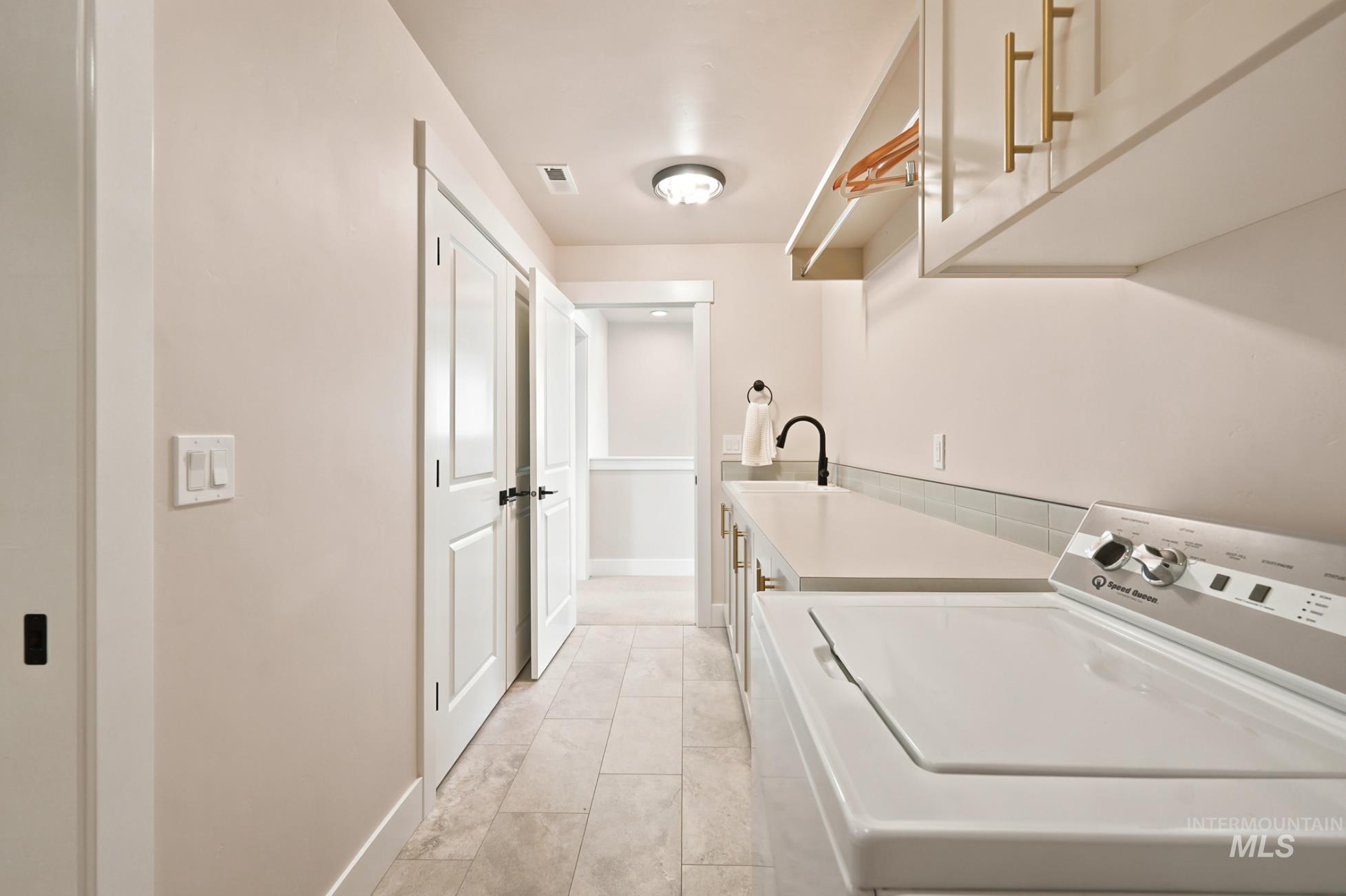 6933 South Zenith Avenue Meridian, ID 83642 - Photo 22 of 34 Laundry room featuring light-toned tile flooring, light neutral walls, white cabinetry with gold-finish hardware, a built-in sink with a matte black faucet, and overhead shelving with a hanging rod