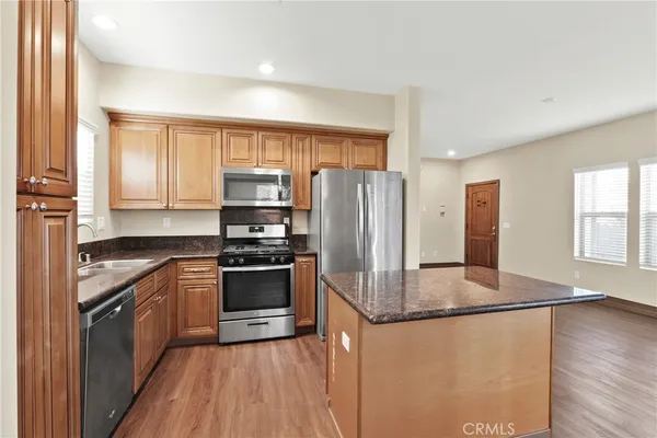 a kitchen with stainless steel appliances granite countertop a refrigerator a stove and a sink with wooden floors