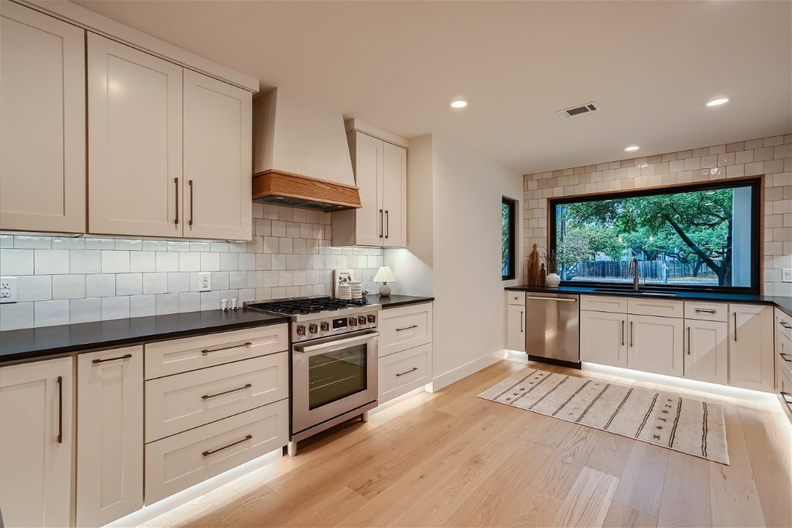 a kitchen with stainless steel appliances granite countertop a stove a sink and white cabinets with wooden floor