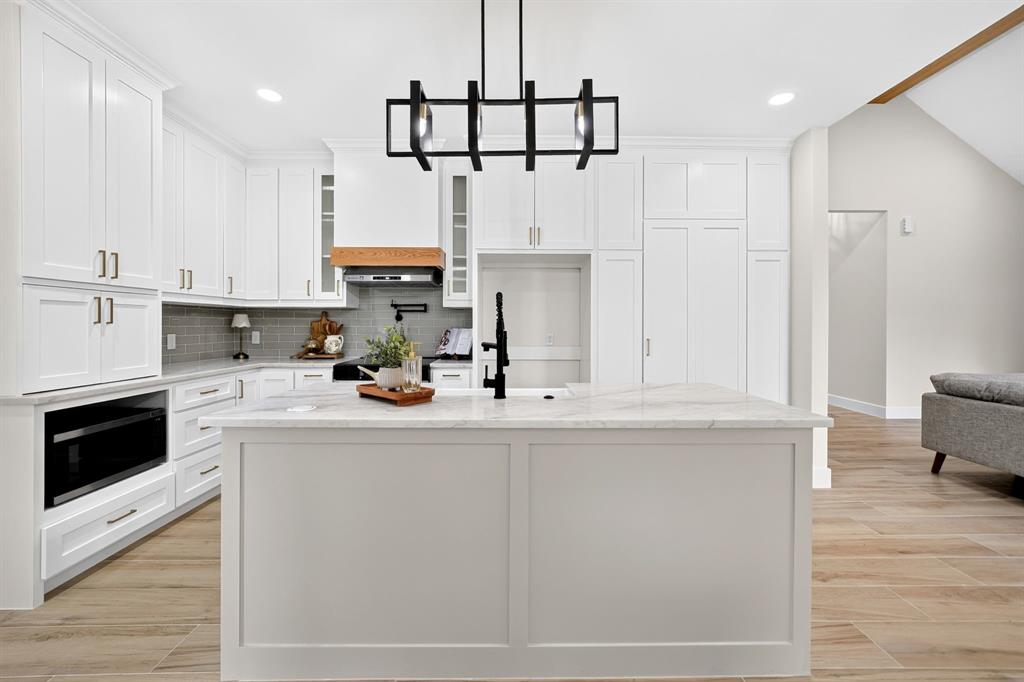 120 Springwood Road Enchanted Oaks, TX 75156 - Photo 20 of 37 White shaker cabinetry with gold-toned hardware, center island featuring a white stone countertop, wood-finish flooring, and a contemporary black chandelier