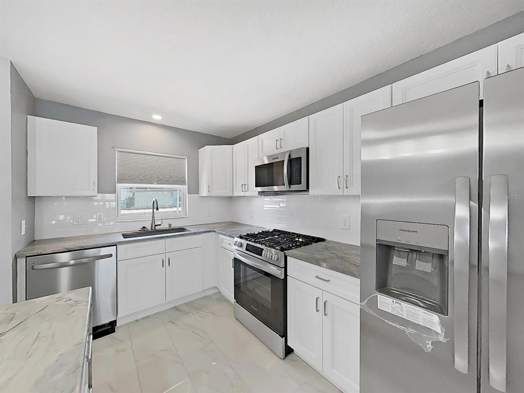 7 Dunoon Place, Unit 104 Dunedin, FL 34698 - Photo 8 of 45 a kitchen with stainless steel appliances granite countertop white cabinets a sink a stove a microwave and a refrigerator