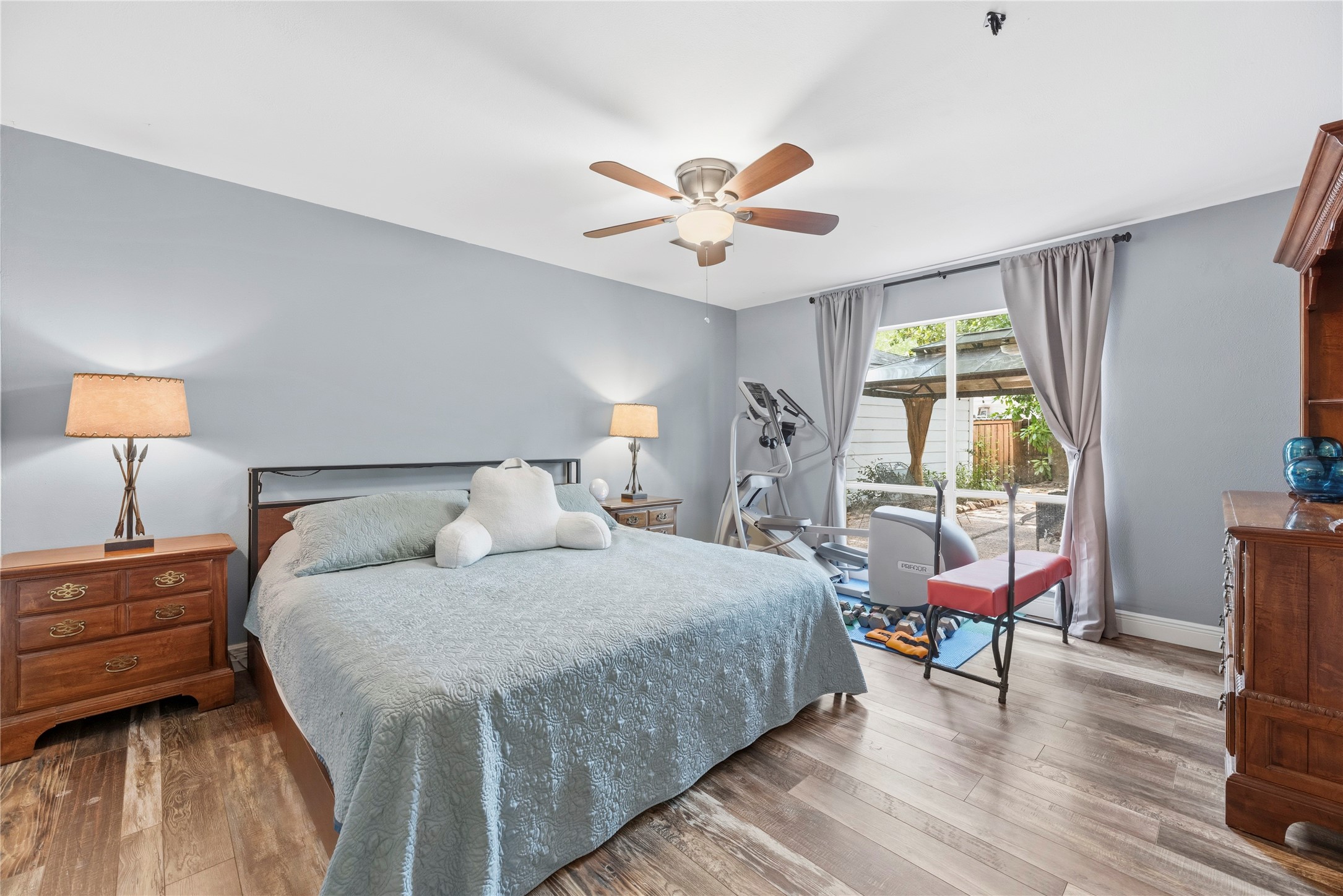 14203 Wickersham Lane Houston, TX 77077 - Photo 12 of 25 Expansive primary bedroom suite showcasing modern wood-look plank flooring, light gray walls, a contemporary ceiling fan, and large windows that frame views of the private backyard.