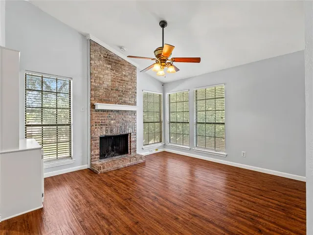 a view of an empty room with wooden floor fireplace and a window