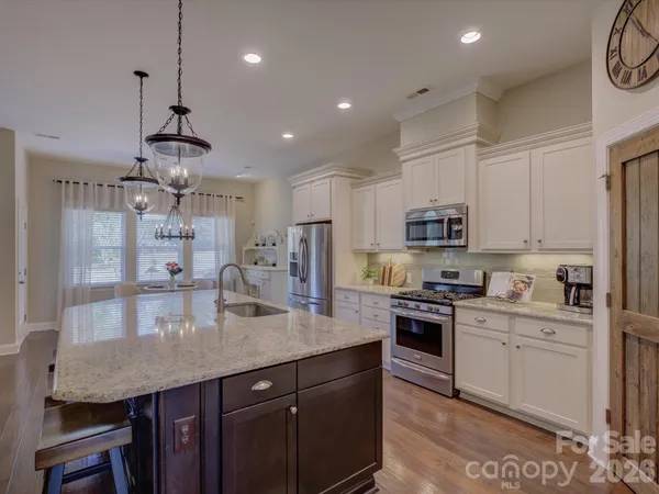 a kitchen with stainless steel appliances granite countertop a sink a stove a refrigerator cabinets and chairs