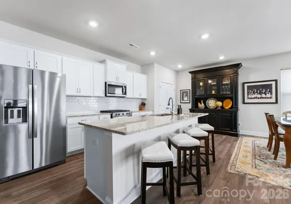a kitchen with stainless steel appliances granite countertop a dining table chairs refrigerator and microwave