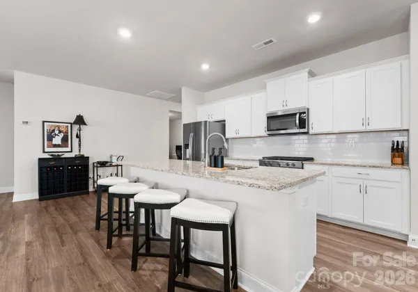 a kitchen with stainless steel appliances granite countertop a stove a sink a microwave a refrigerator a dining table and chairs with wooden floor