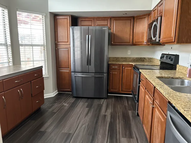 a kitchen with granite countertop wooden floors stainless steel appliances a sink and a window