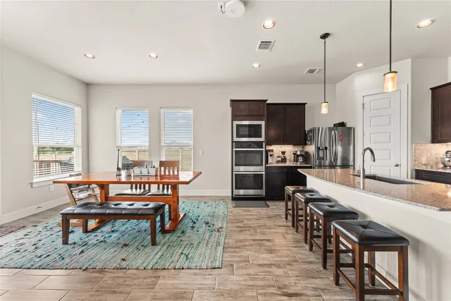 a kitchen with stainless steel appliances granite countertop a stove top oven a sink dishwasher a dining table and chairs with wooden floor