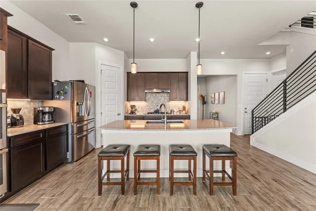 a kitchen with stainless steel appliances granite countertop a stove a refrigerator a kitchen island a dining table and chairs with wooden floor