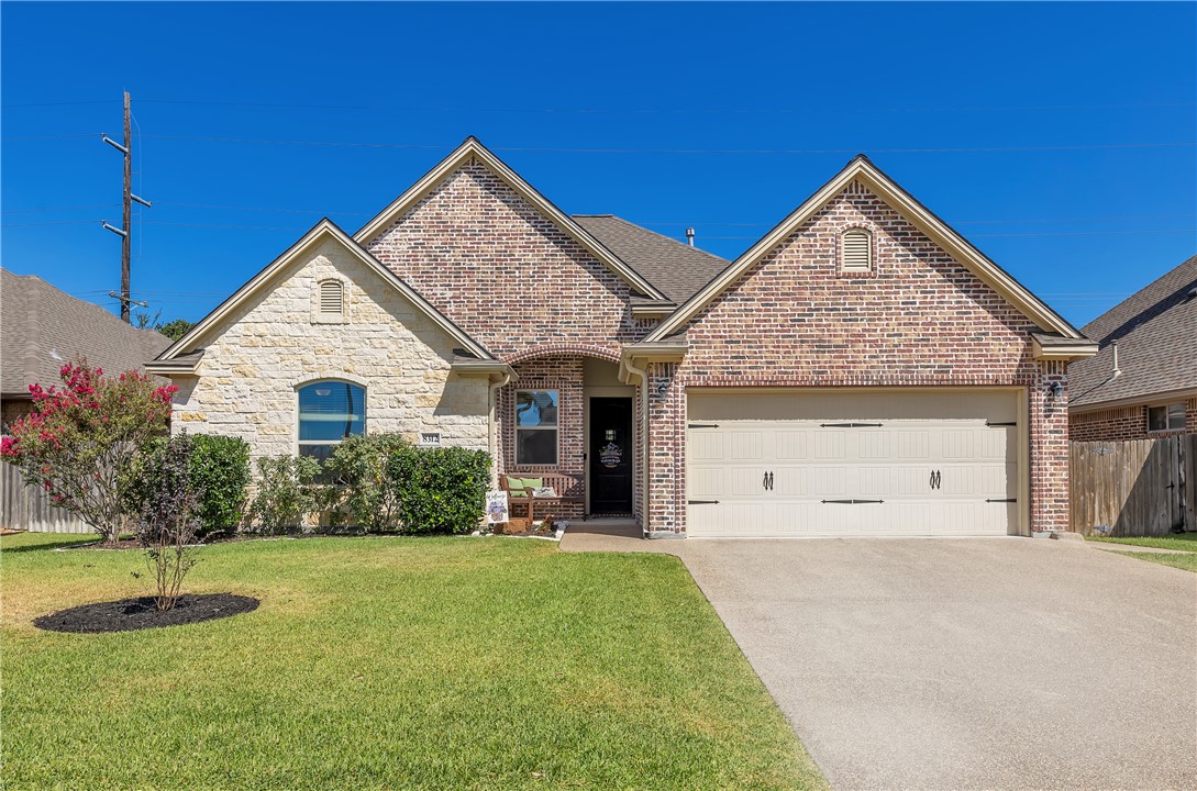 8312 Raintree Drive College Station, TX 77845 - Photo 1 of 30 Brick and stone exterior featuring a two-car garage, pitched roofline, and established front landscaping