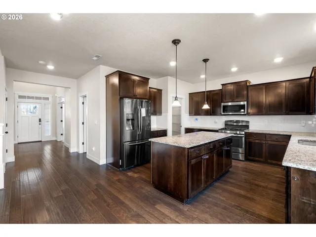 a kitchen with stainless steel appliances granite countertop a stove a refrigerator a sink a oven with wooden cabinets and floor