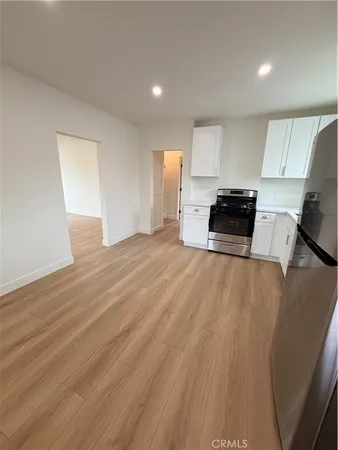 a kitchen with stainless steel appliances a stove a refrigerator a sink a microwave oven with white cabinets and wooden floor