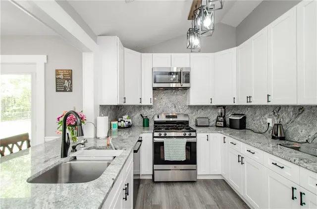 a kitchen with granite countertop a sink stainless steel appliances and white cabinets