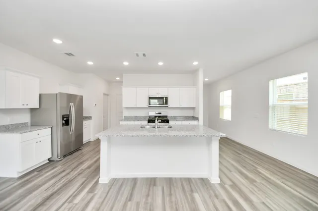 a large kitchen with stainless steel appliances kitchen island a large counter top and a stove top oven with wooden floor