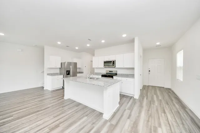 a large white kitchen with kitchen island a sink a center island stainless steel appliances and a counter space