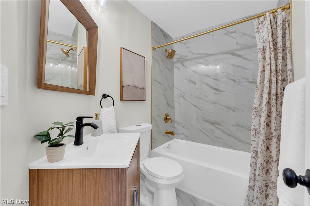 18155 Libby Road Maple Heights, OH 44137 - Photo 26 of 32 Bathroom featuring a wood-finish vanity with a white countertop and matte black faucet, a framed mirror, a bathtub with a shower enclosure, full-height marble-style wall tiling, and gold-tone fixtures
