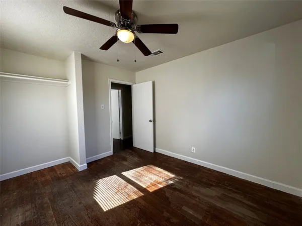 a view of an empty room with wooden floor and a ceiling fan