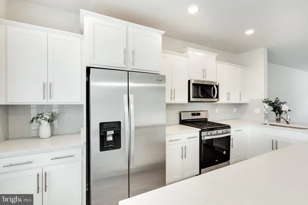 a large kitchen with stainless steel appliances a large counter top a stove a refrigerator cabinets and a window