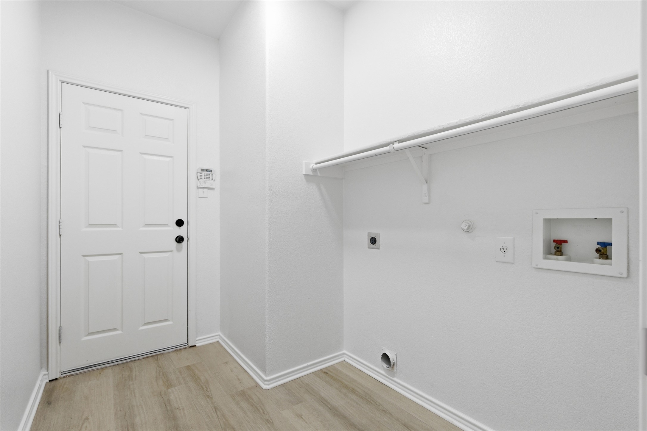 461 Hot Spring Valley Buda, TX 78610 - Photo 20 of 25 Utility space featuring light wood-style flooring, a white paneled door, and a white wall shelf with a clothing rod