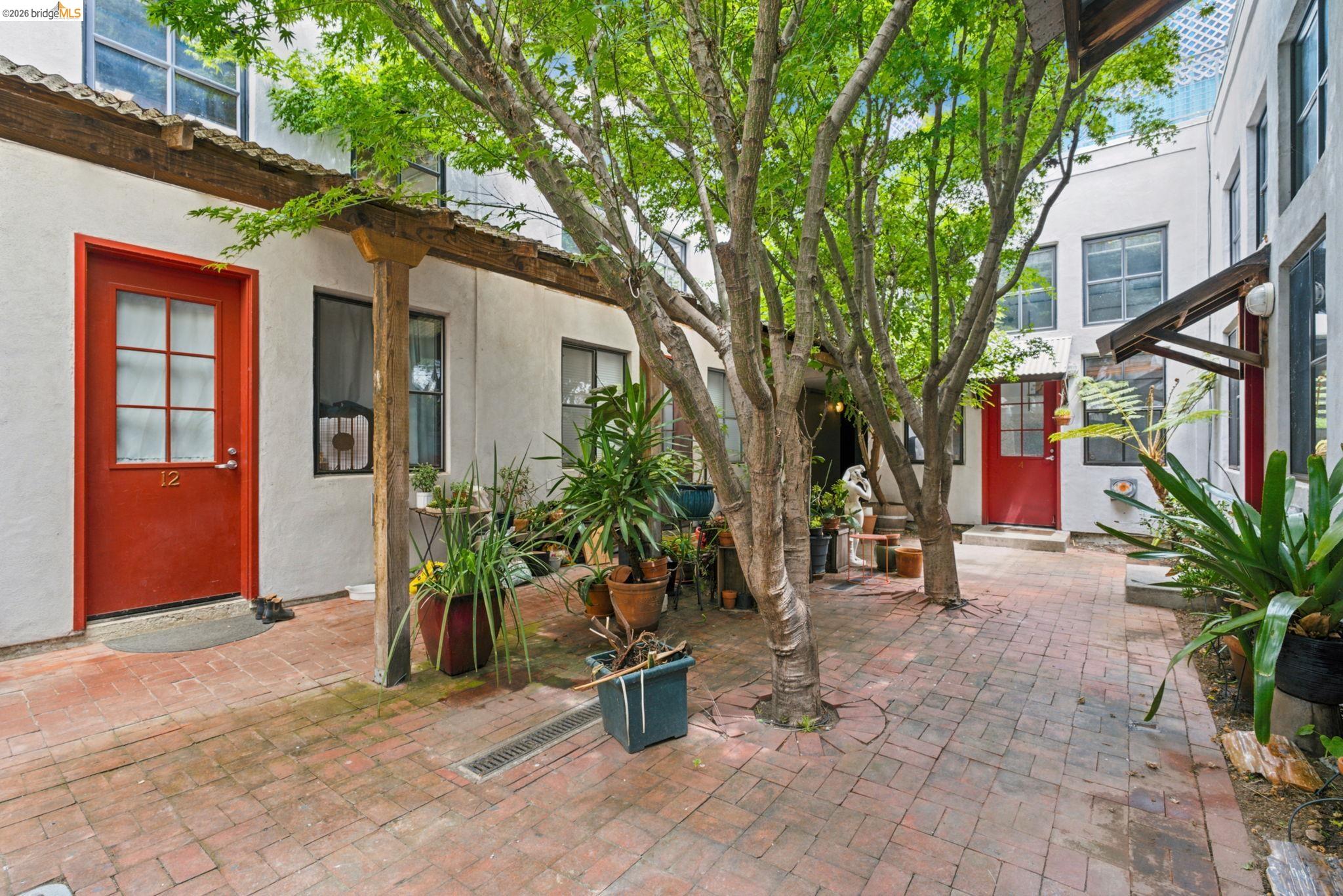 1920 Union Street, Unit 9 Oakland, CA 94607 - Photo 32 of 35 Brick paver courtyard featuring multiple mature trees providing shade and a red entry door with glass panels