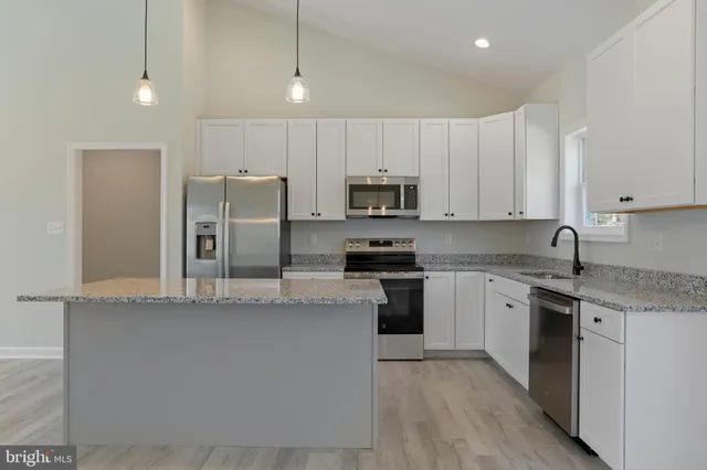 a kitchen with stainless steel appliances granite countertop a stove a sink a refrigerator and white cabinets with wooden floor