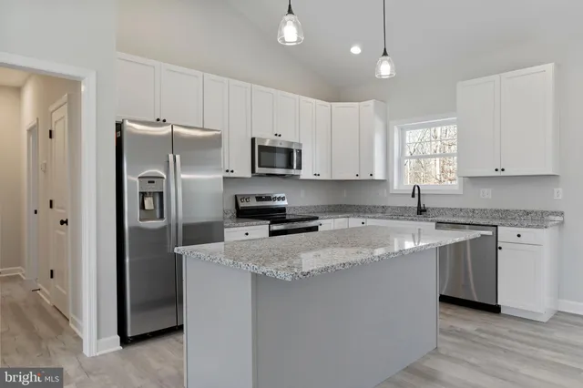 a kitchen with stainless steel appliances granite countertop a refrigerator a stove a sink and white cabinets