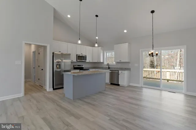 a large kitchen with stainless steel appliances granite countertop a refrigerator a sink dishwasher a oven and a kitchen island with wooden floor