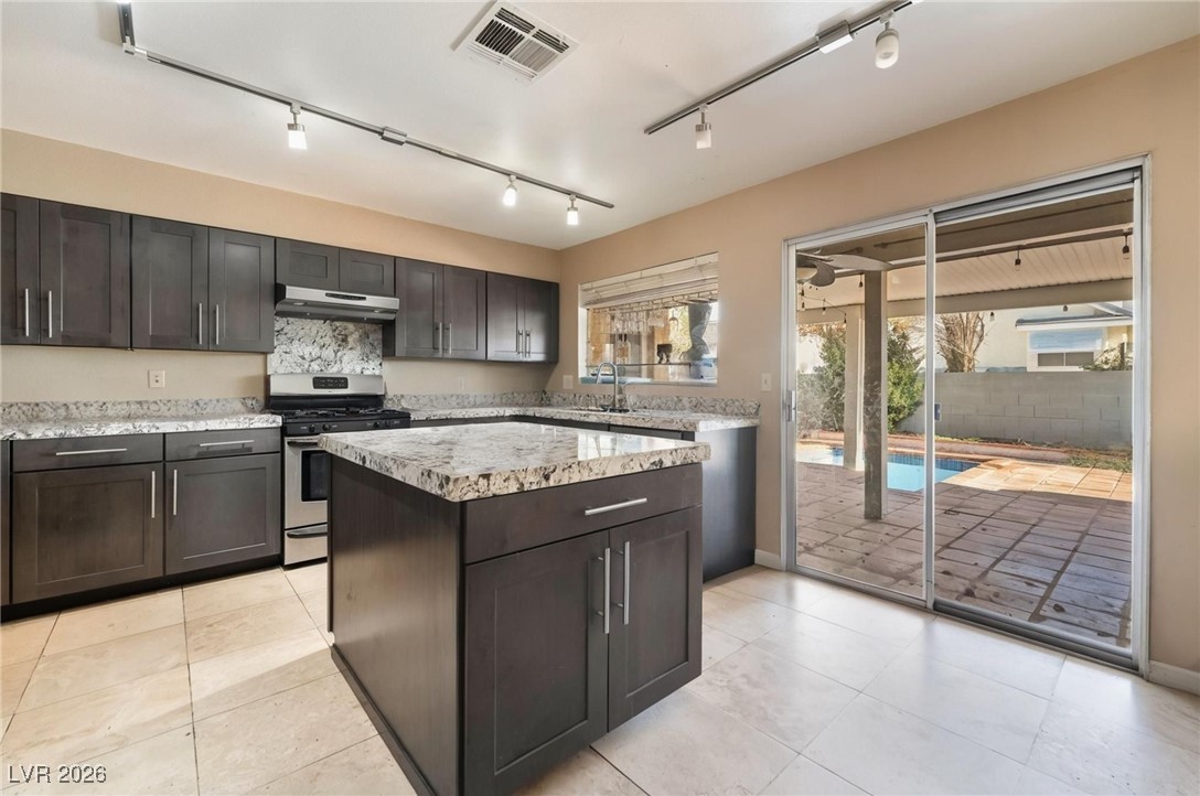 300 Redondo Street Henderson, NV 89014 - Photo 3 of 29 Kitchen with stainless steel gas stove, light stone counters, tasteful backsplash, track lighting, and under cabinet range hood
