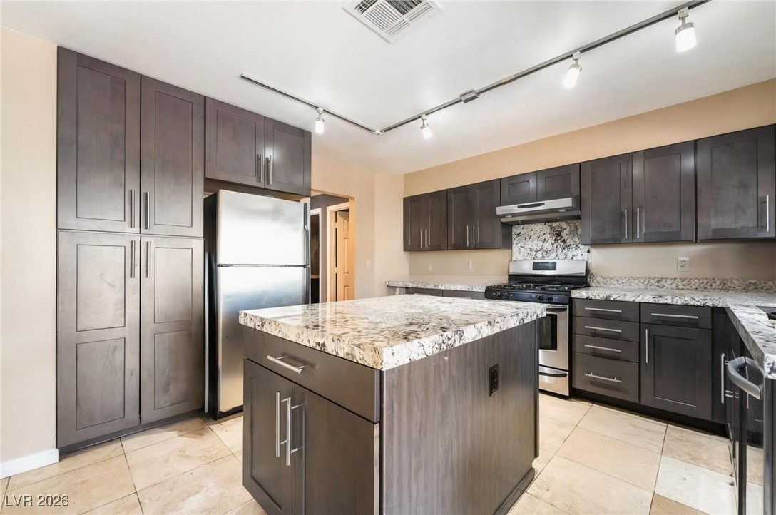 300 Redondo Street Henderson, NV 89014 - Photo 4 of 29 Kitchen with stainless steel appliances, backsplash, dark brown cabinets, a kitchen island, and under cabinet range hood
